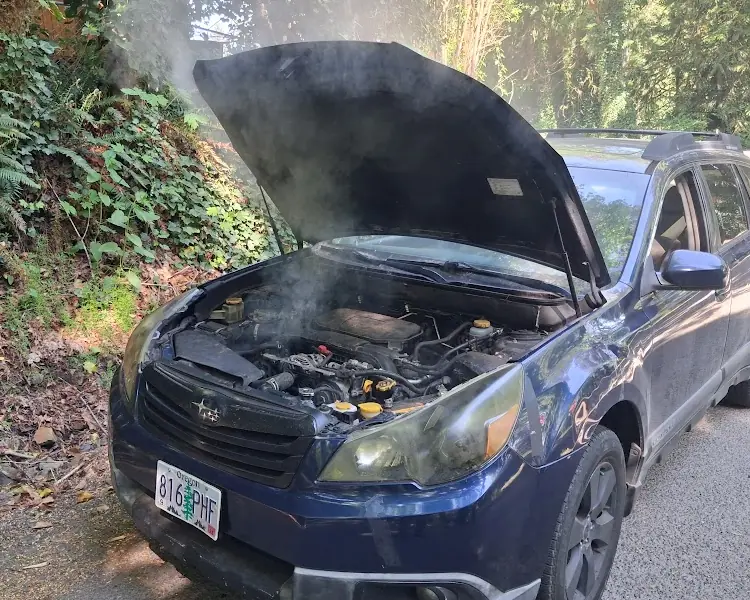 Subaru with its hood open and steam rising from the engine bay during a roadside repair.